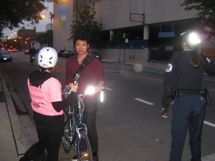 A bike ambassador and a police officer give a cyclist a free headlight during an enforcement event. Photo: CDOT