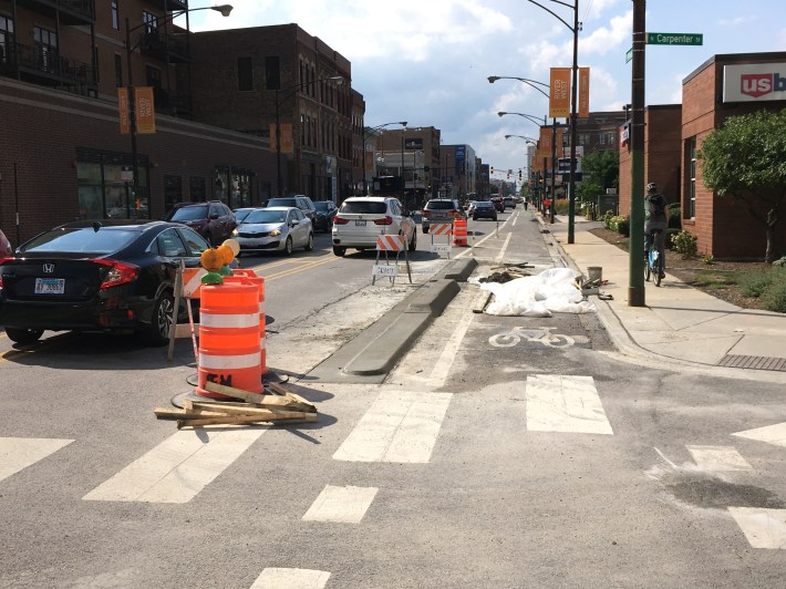 A low curb at Carpenter St allows motorists to make wide fast turns. An alternative could be to have the curb the same height and to ban the 270 degree turn from southbound Carpenter to northbound Milwaukee. It's common for motorists on Carpenter to drive past the stop bar and nose into the bike lane as people are cycling.