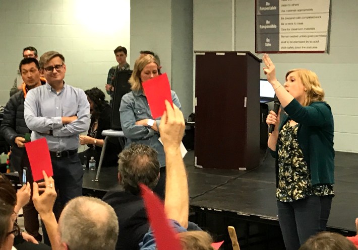 Jacob Huebert stands by as his wife Allison voices opposition to the TOD at the community meeting; other residents raise red cards to express disagreement with her talking points. Photo: John Greenfield