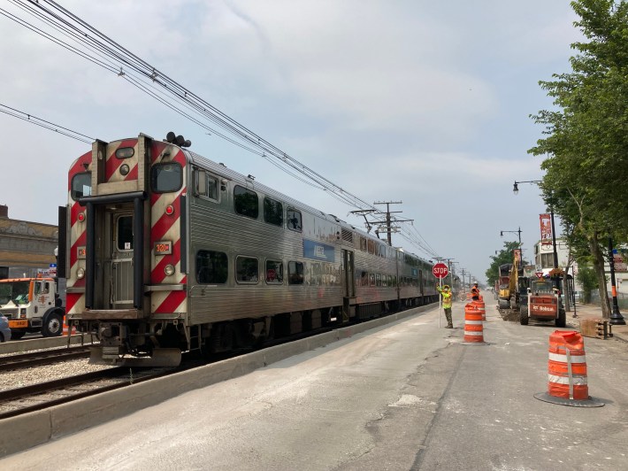 A Metra Electric train passes by a crew working on the 71st Street streetscape. Photo: John Greenfield