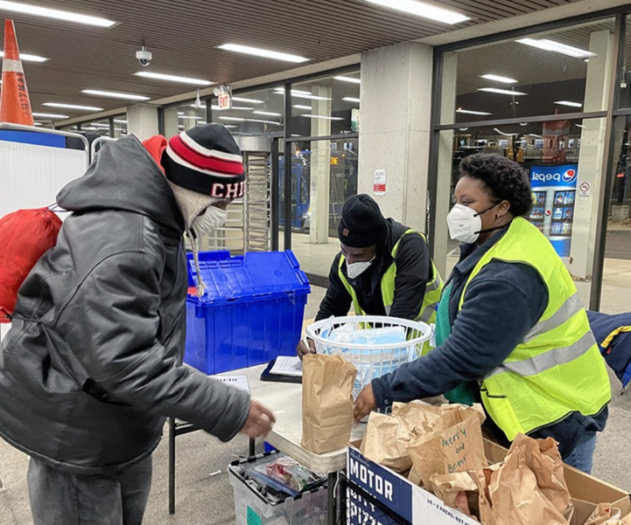A resident receives a sack supper from Kyanna Johnson, an outreach worker for The Night Ministry, at a CTA Blue Line station. Photo: The Night Ministry