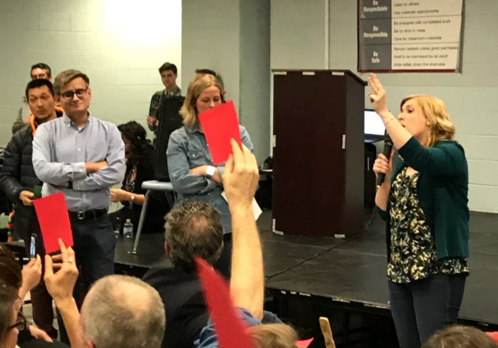 Jacob Huebert stands by as his wife Allison voices opposition to the TOD plan at a community meeting on the project; other residents raise red cards to express disagreement with her talking points. Photo: John Greenfield
