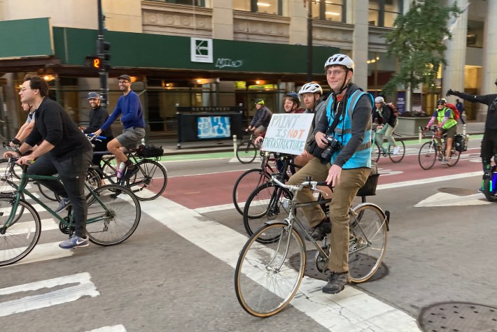 A rider with a "Paint Is Not Infrastructure" sign. Streetsblog cofounder Steve Vance is in the background in a blue shirt. Photo: John Greenfield