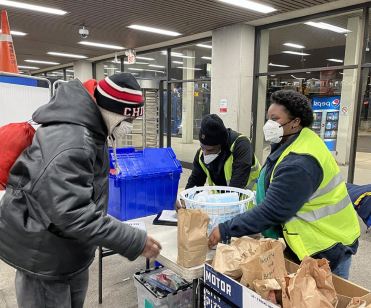 A resident receives a sack supper from Kyanna Johnson, an outreach worker for The Night Ministry, at a CTA Blue Line station. Photo: The Night Ministry